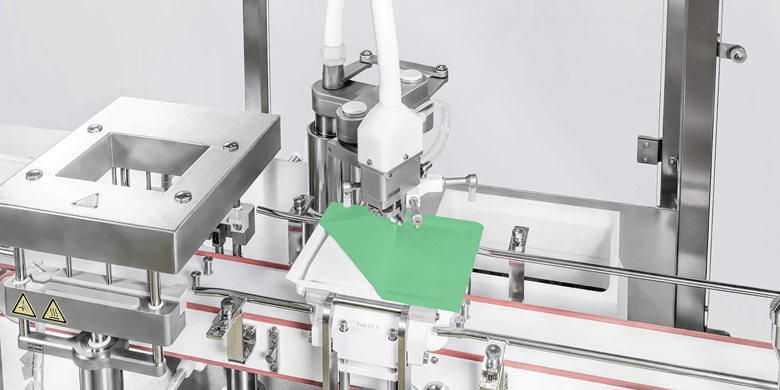 Syntegon automated machine applying a sterile film to a ready-to-use (RTU) container in a pharmaceutical processing line. High-precision robotic arm ensures sterile and efficient sealing for safe drug packaging.